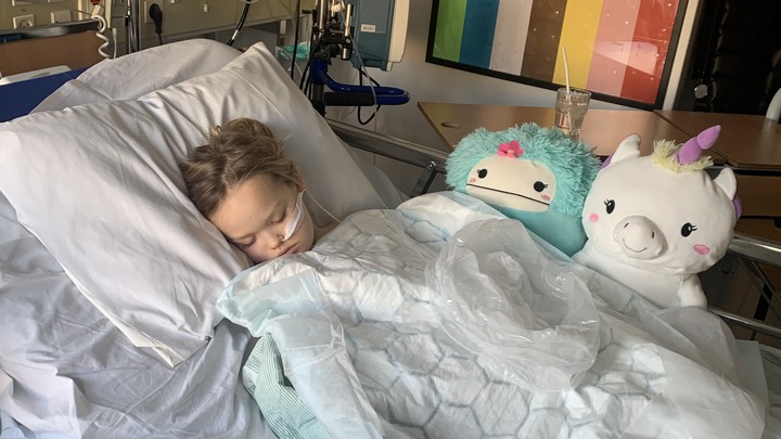Alice ligger i en sjukhuss&auml;ng och sover, med sond.