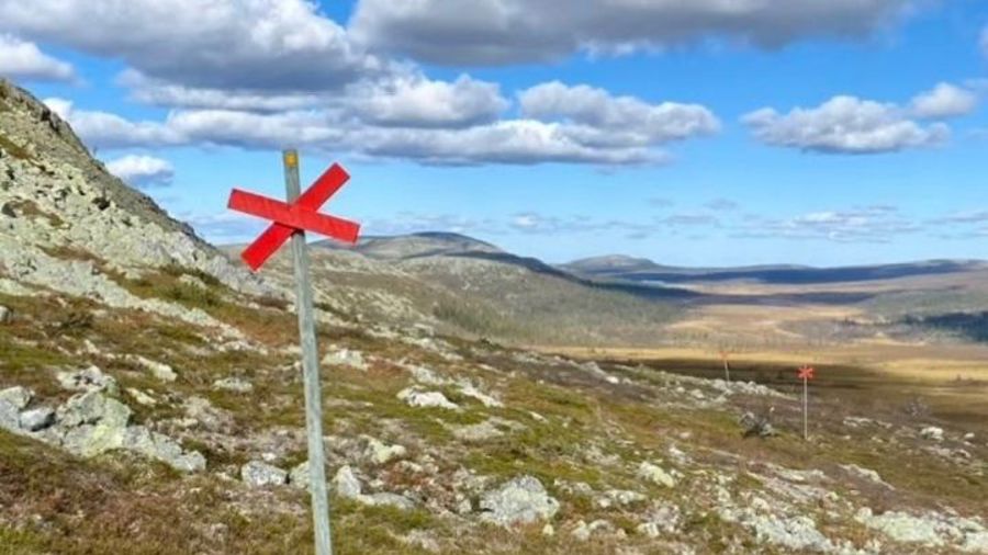 Från svenska fjällvärlden med fjäll i fjärran. Stolpe med rött kryss i förgrunden. Blå himmel med moln.